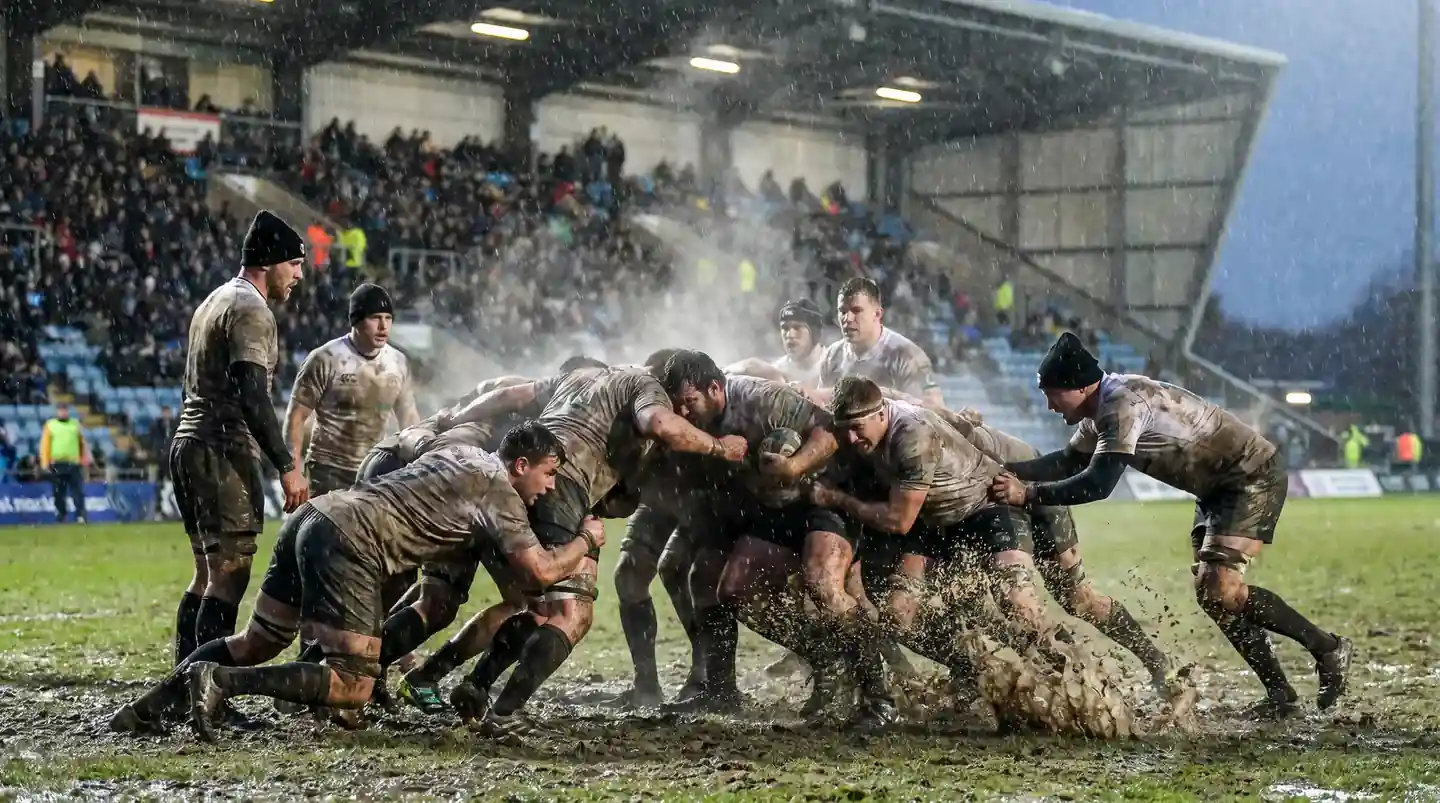 Rugby players contesting a scrum on a waterlogged pitch during heavy rain